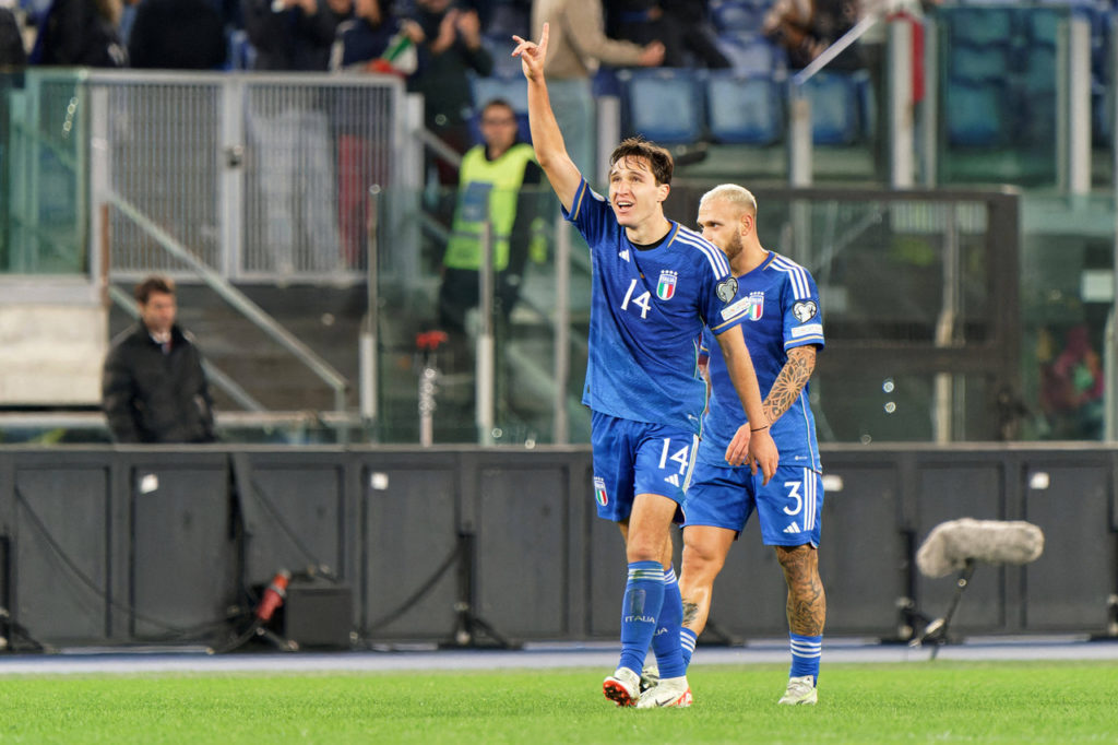 Chiesa, atacante da seleção italiana, vestindo a camisa da equipe de seu país e erguendo um dos braços durante partida no Estádio Olímpico de Roma.