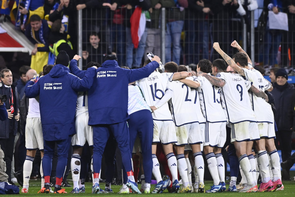 Jogadores da seleção italiana reunidos e abraçados dentro do campo após uma partida da equipe.