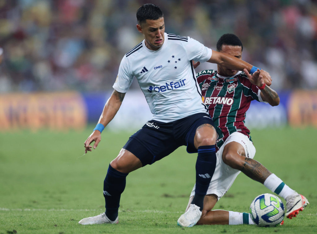 Mateus Vital, meia do Cruzeiro, tenta manter a bola dominada enquanto um adversário tenta roubá-la.